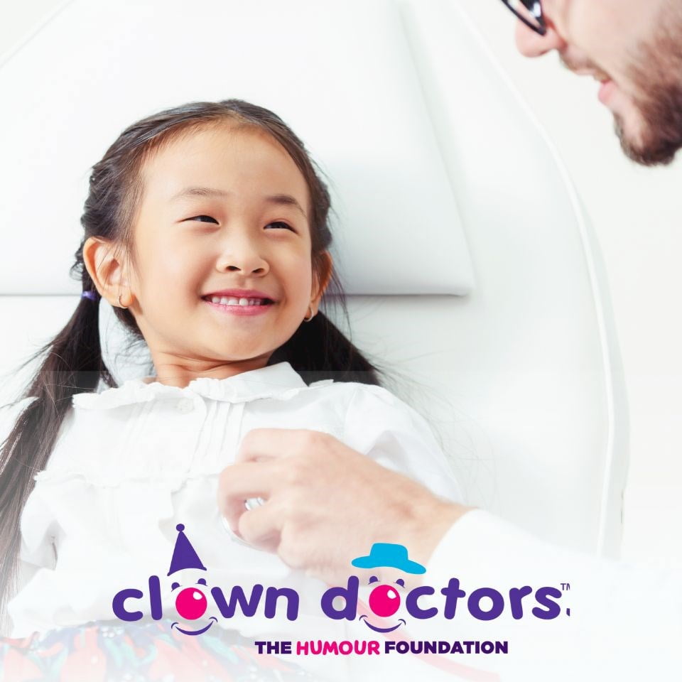 Little girl smiling, being examined by a doctor and Clown doctors' logo
