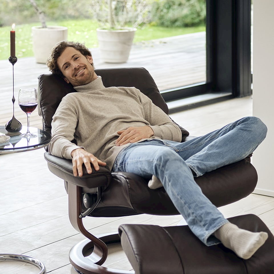 Man laying in a Stressless® recliner in front of a large window