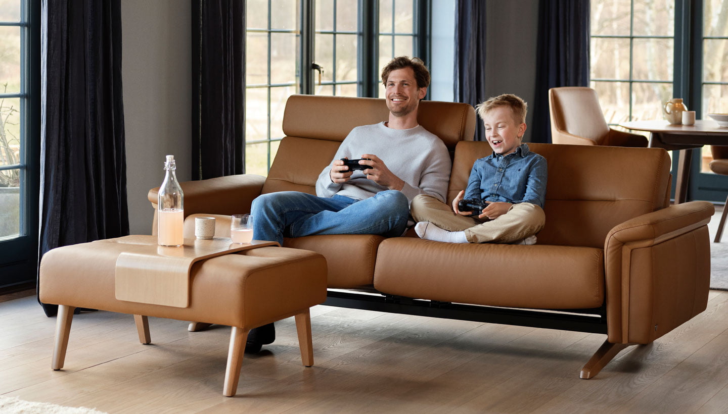 Vader en zoon spelen videospelletjes op een Stressless Stella bank